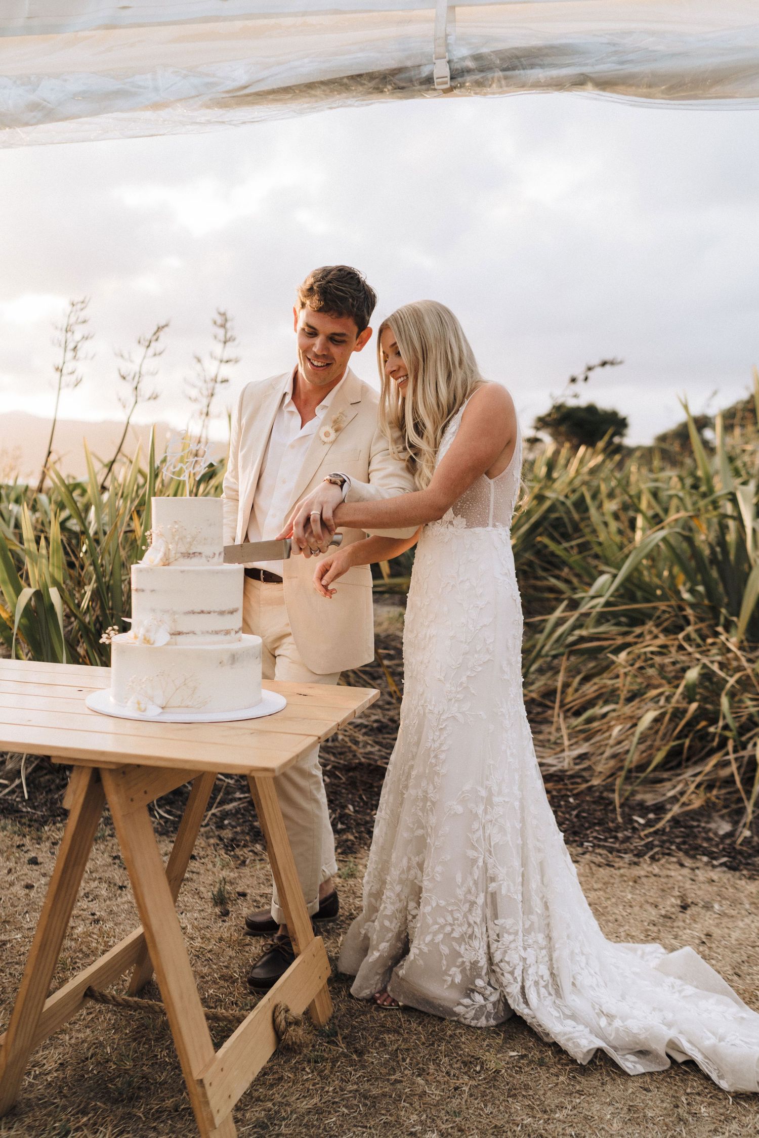 Newlyweds cutting their white wedding cake together at an outdoor reception.