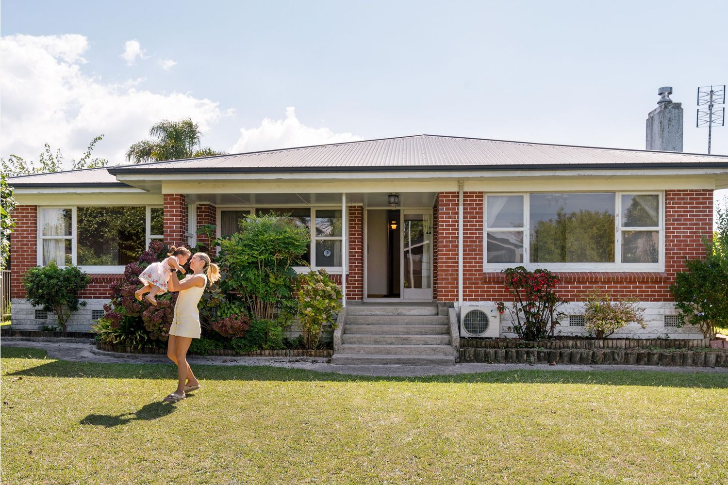 A classic brick ranch house with front yard and entrance steps in warm sunlight.