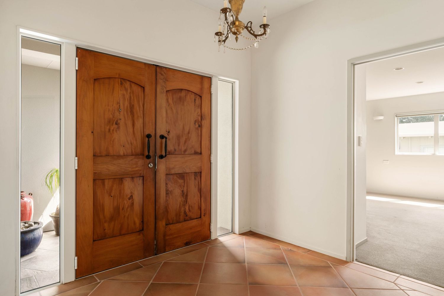 Elegant entryway with natural wooden double doors, terra cotta flooring, and a vintage chandelier.