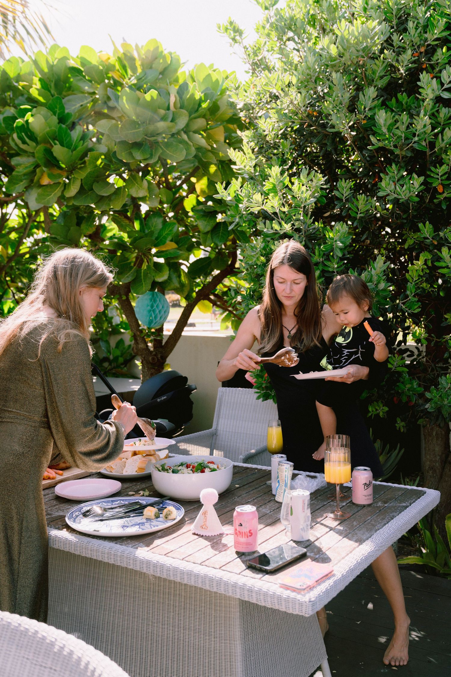 Group dining at an outdoor table with white wicker furniture surrounded by tropical greenery.