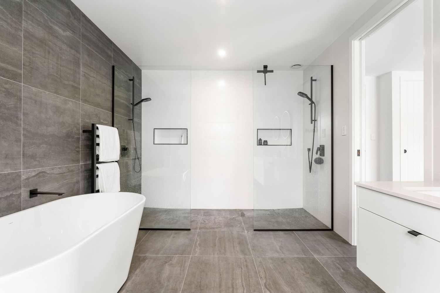 Modern minimalist bathroom with freestanding tub, gray tile floors, white walls and dual shower heads.