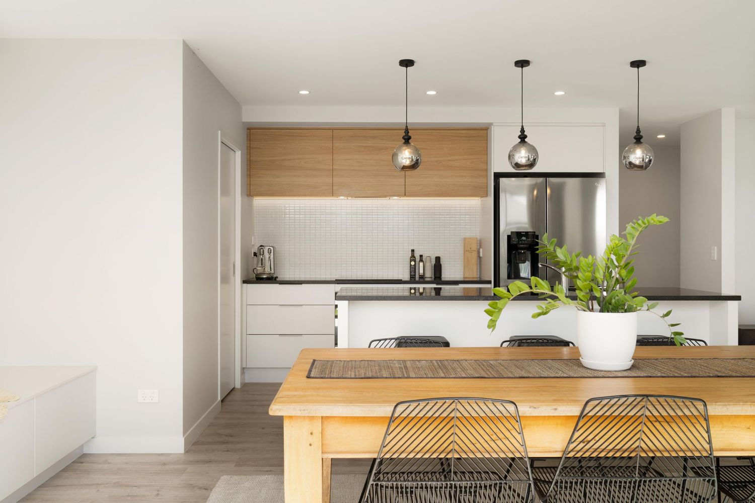 Contemporary white kitchen featuring wooden dining table, black wire chairs and stylish pendant lighting.