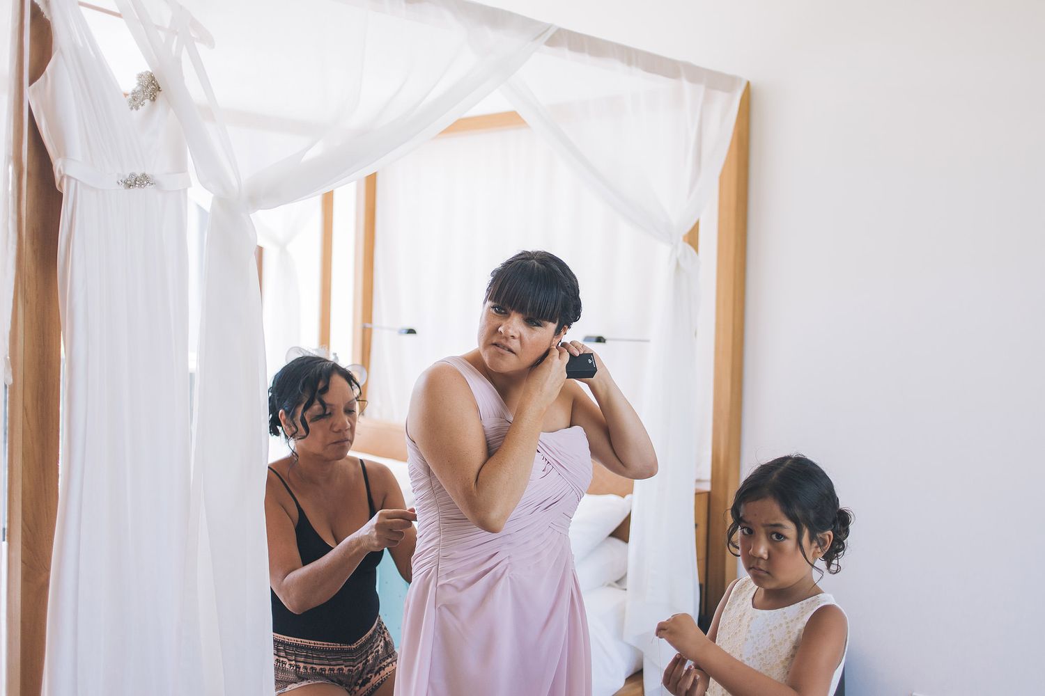 Wedding preparation scene with white dresses and people getting ready in bright room.