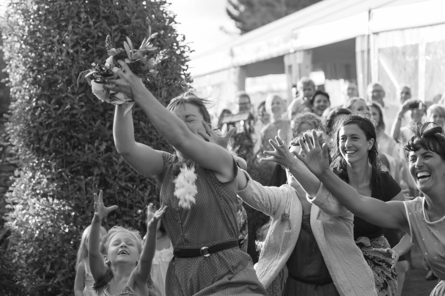 Enthusiastic crowd raises their hands in celebration at an outdoor event with trees in the background.