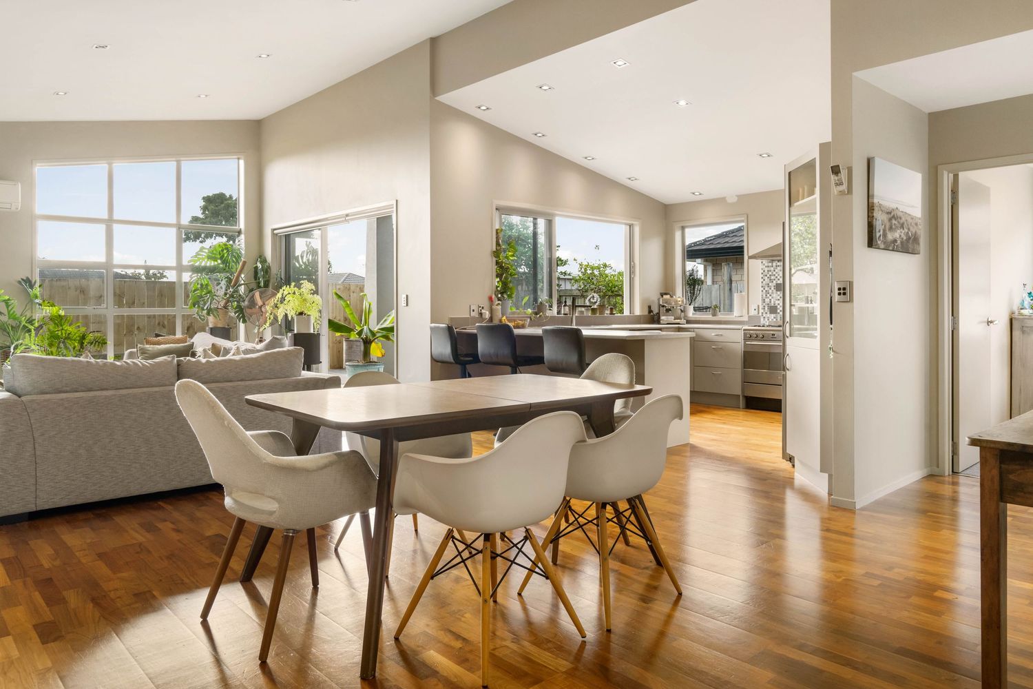 Modern dining room with white chairs around wooden table features glossy hardwood floors and large windows overlooking city view.