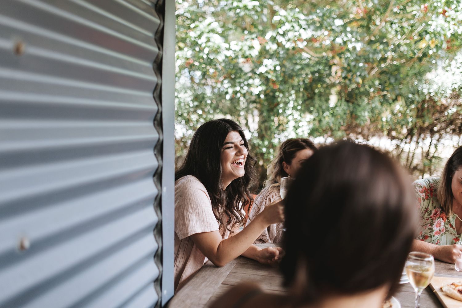 Group of friends gather for outdoor dining and conversation on a sunny afternoon at a rustic table setting.