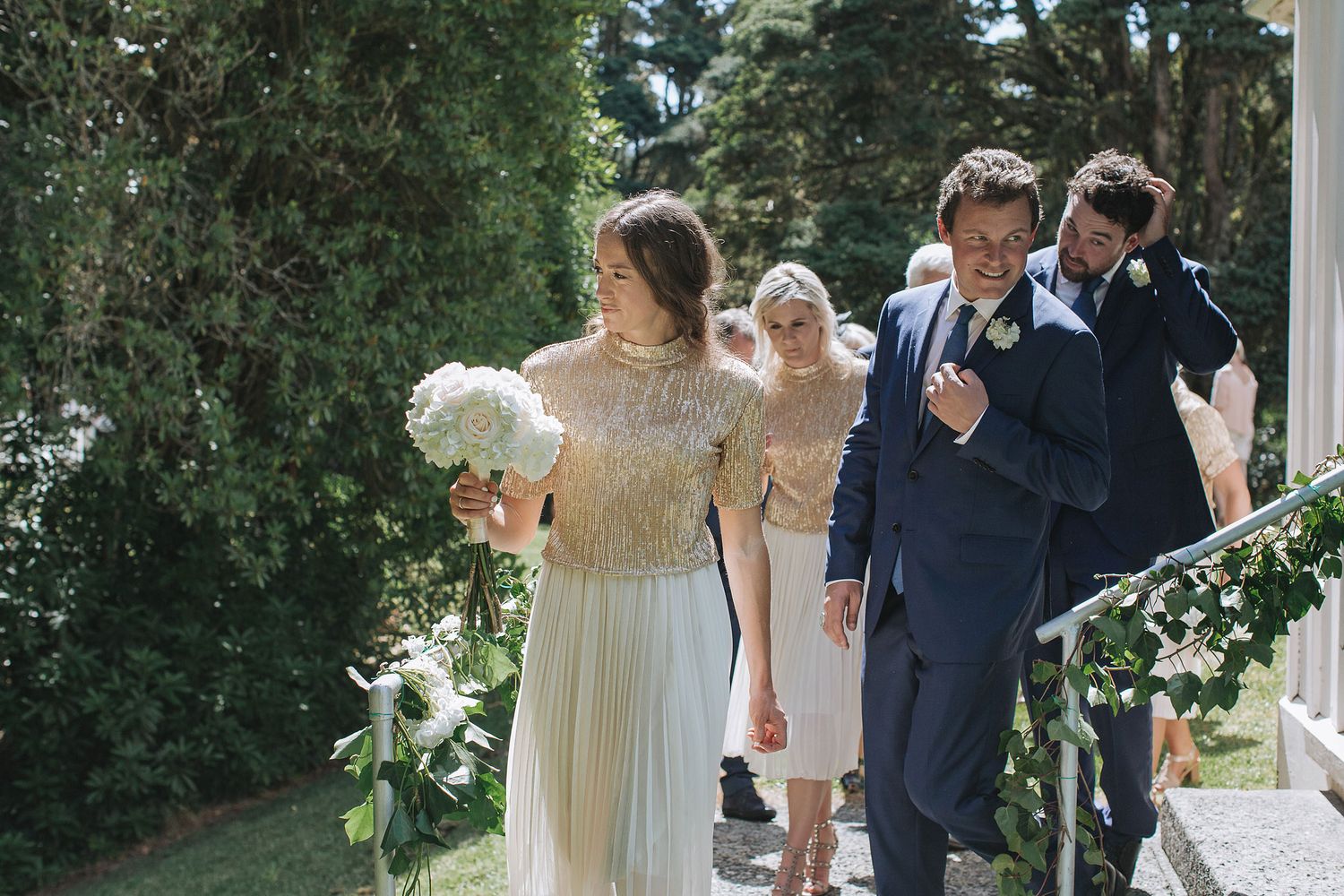 Wedding party gathered outdoors with umbrellas while celebrating during a gentle summer rain shower.