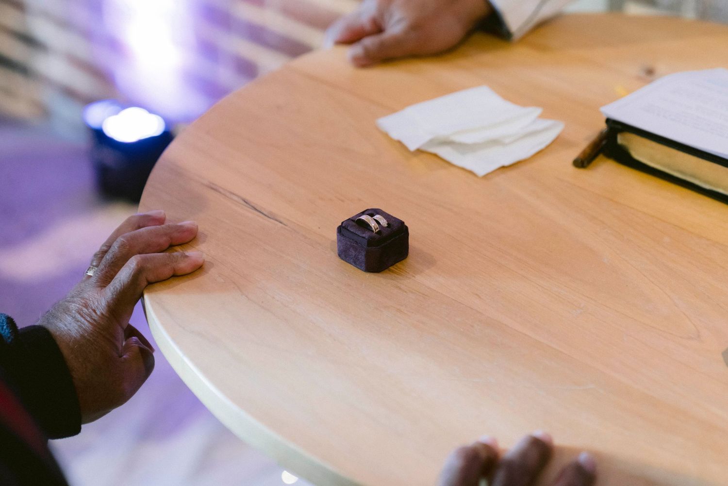 A small black button or electronic device sits on a wooden table surface with blue lighting in the background.