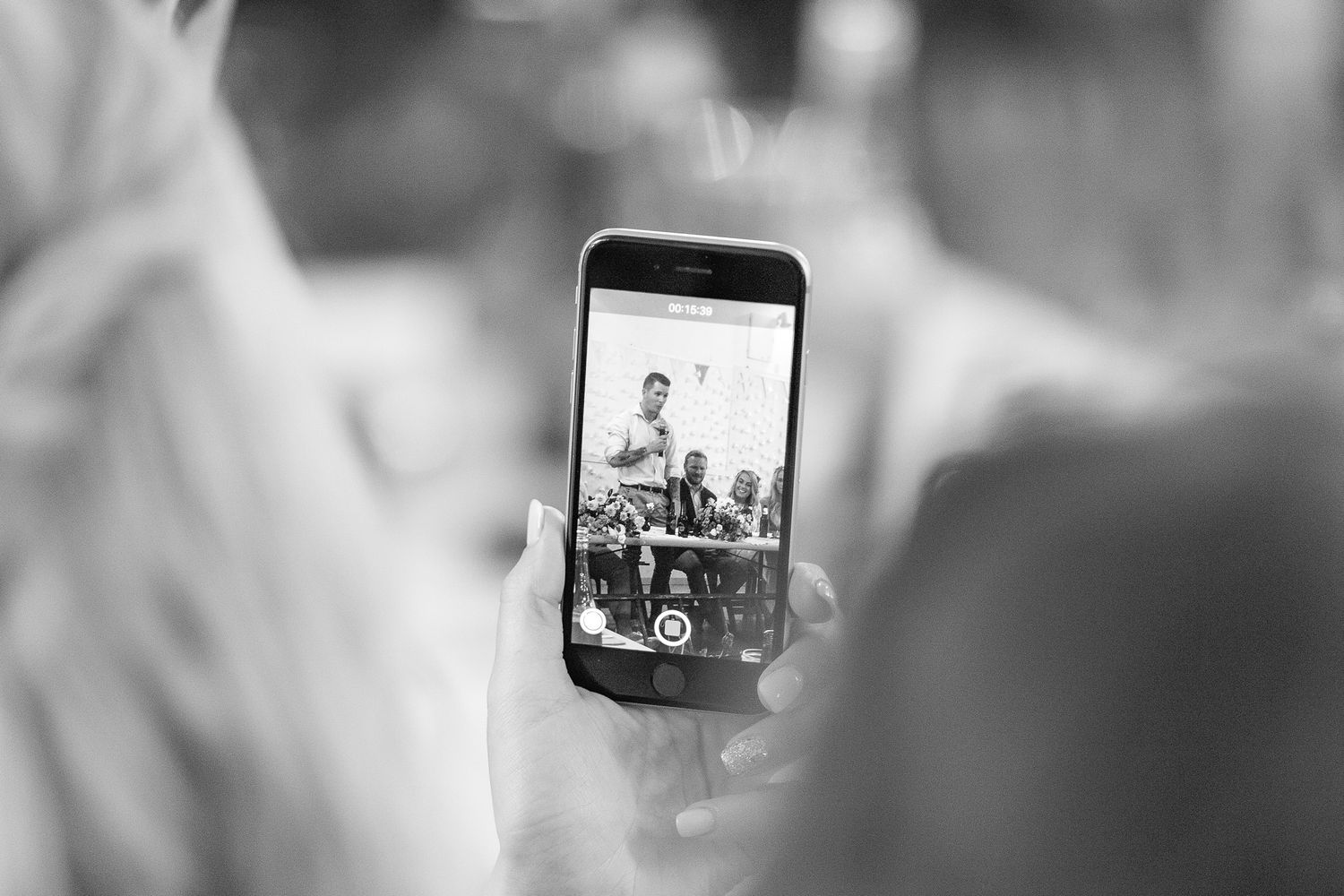 A smartphone held in hand displays a photo being taken in black and white against a blurred background.