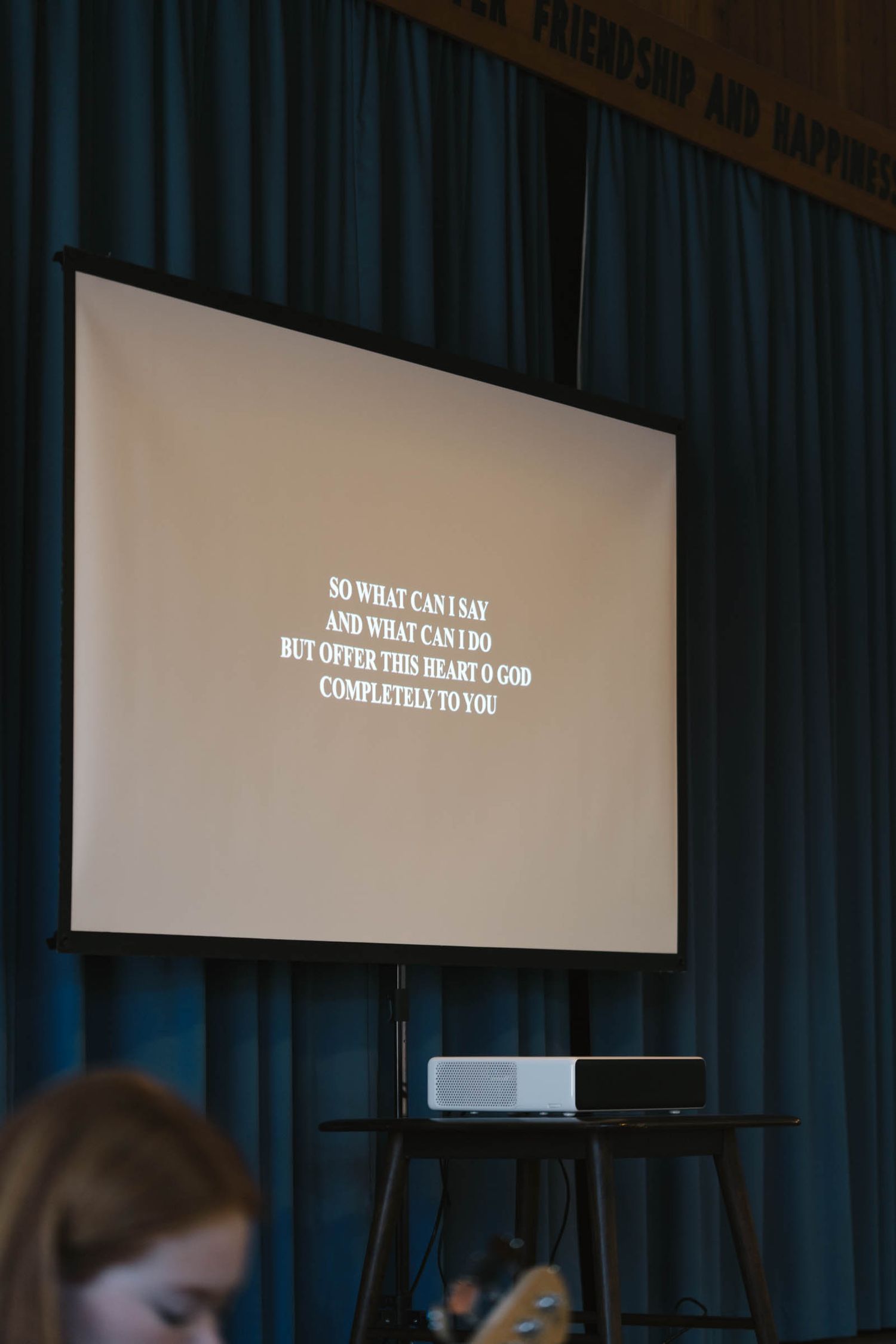 A projection screen displaying text in a church auditorium with blue curtains.