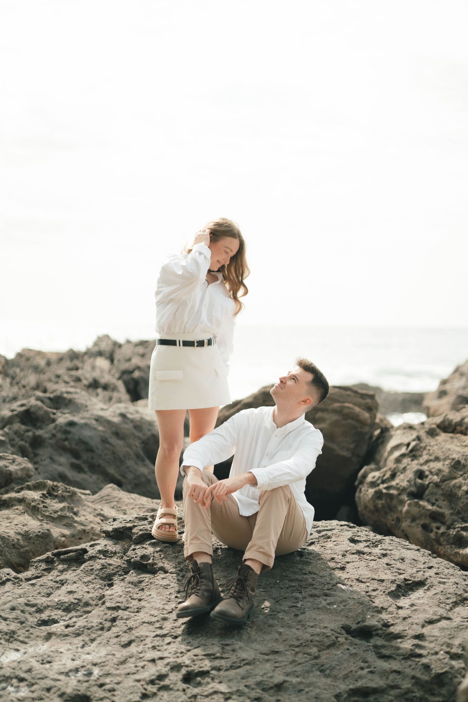Romantic couple sitting together on dark rocky cliffs by the ocean.