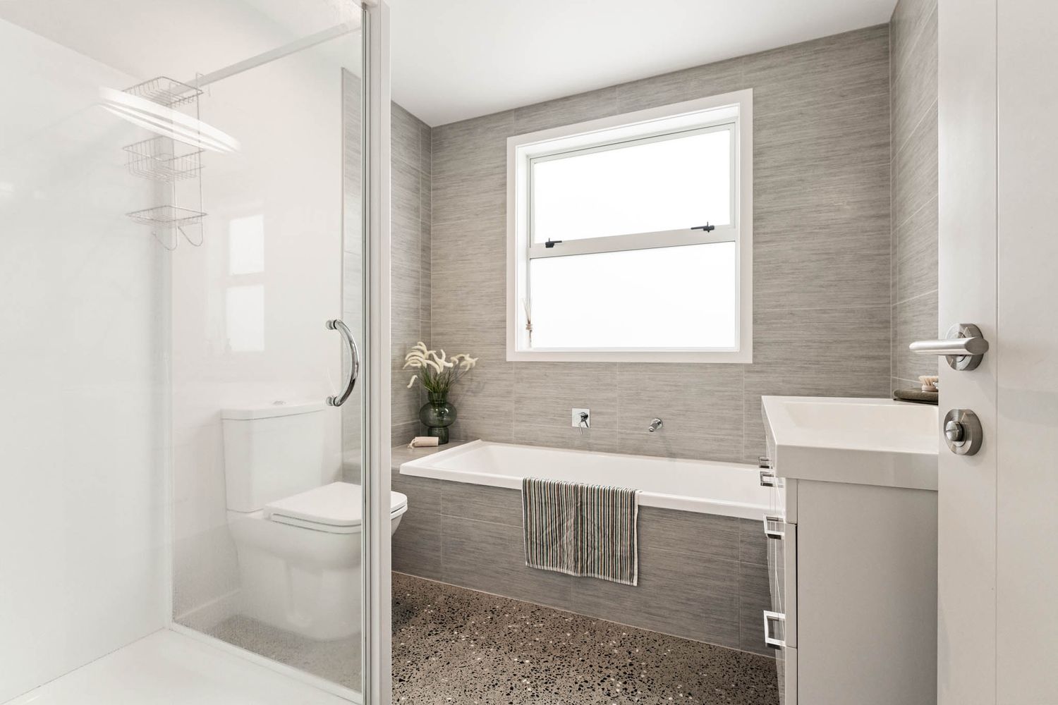 Modern bathroom interior with glass shower enclosure, gray tile walls, and white fixtures in a minimalist design.