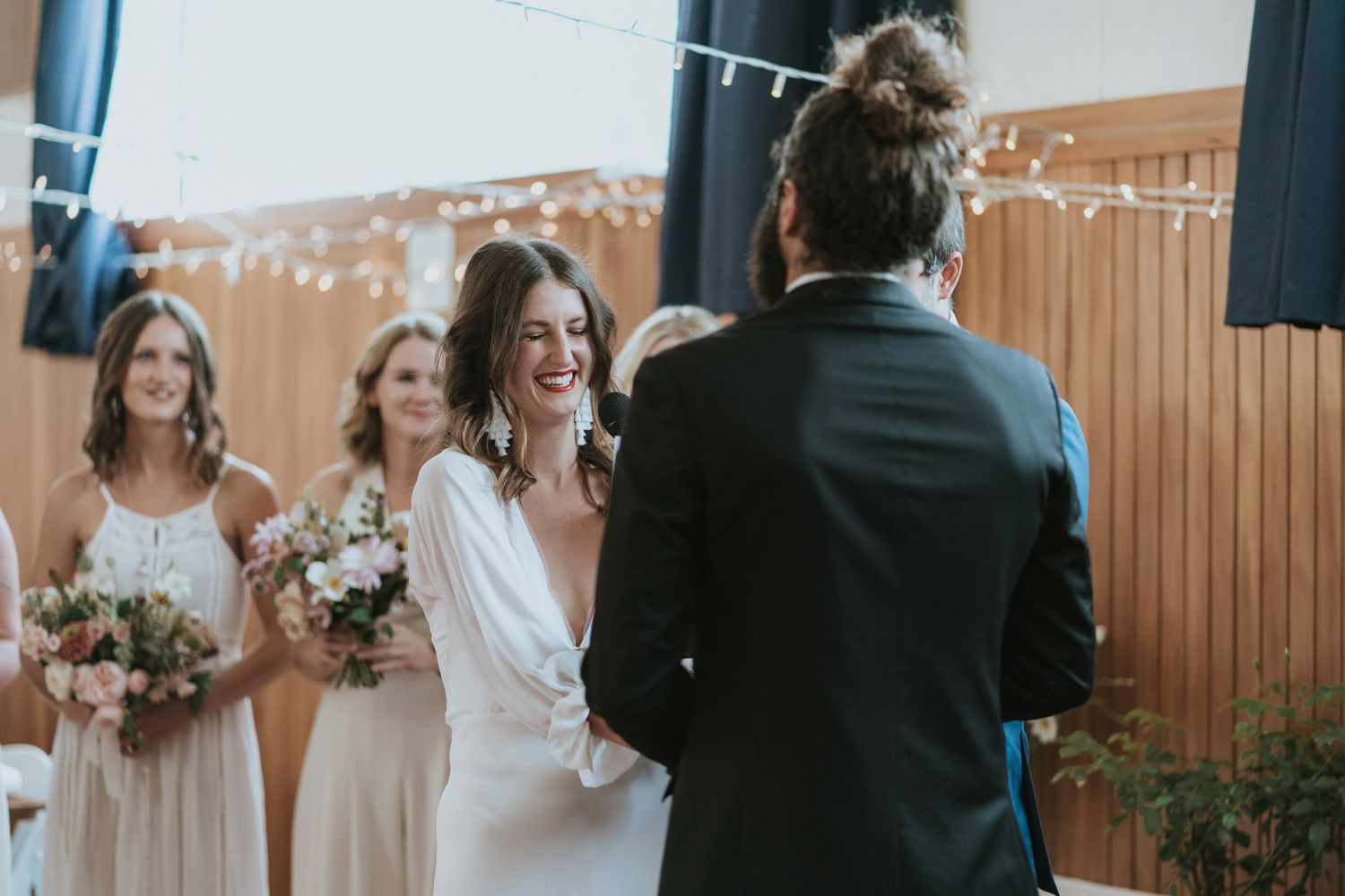 A joyful group in white and cream wedding attire exchange vows during an outdoor ceremony.