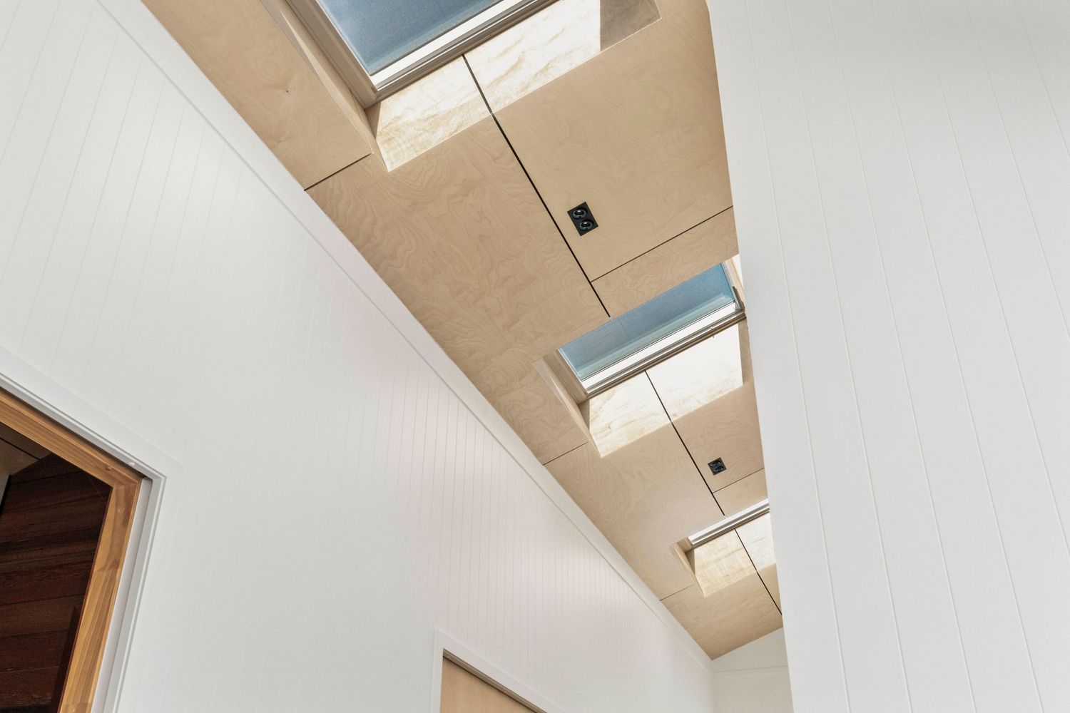 Modern interior hallway with multiple rectangular skylights set in wooden framed recesses along the ceiling.