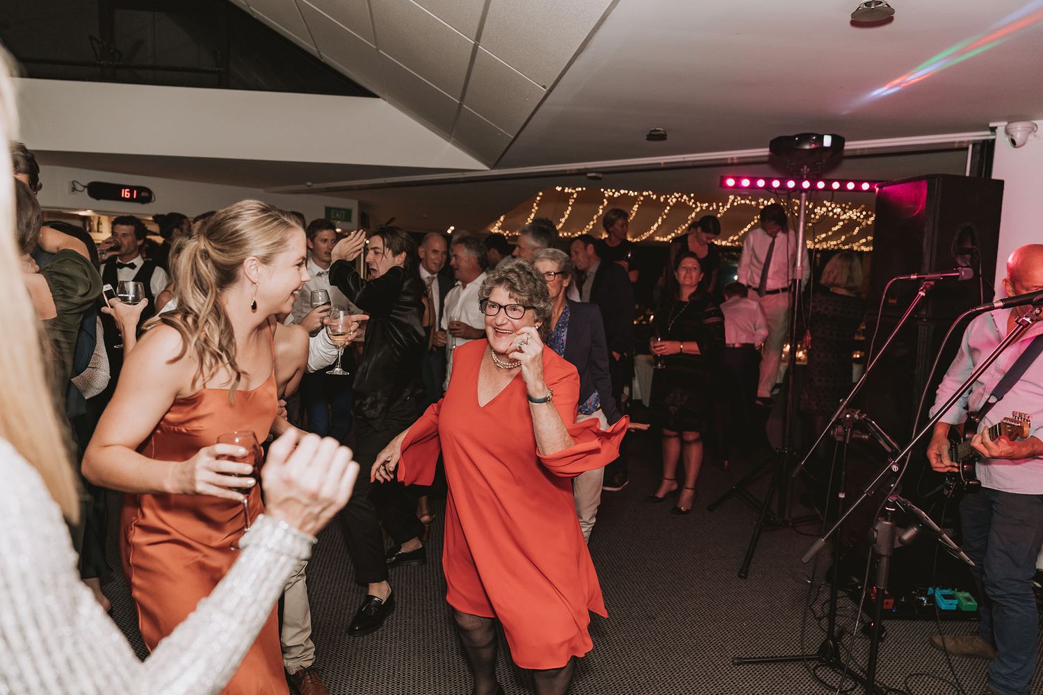 People dance and celebrate at a wedding reception with ambient lighting and energetic atmosphere on the dance floor.