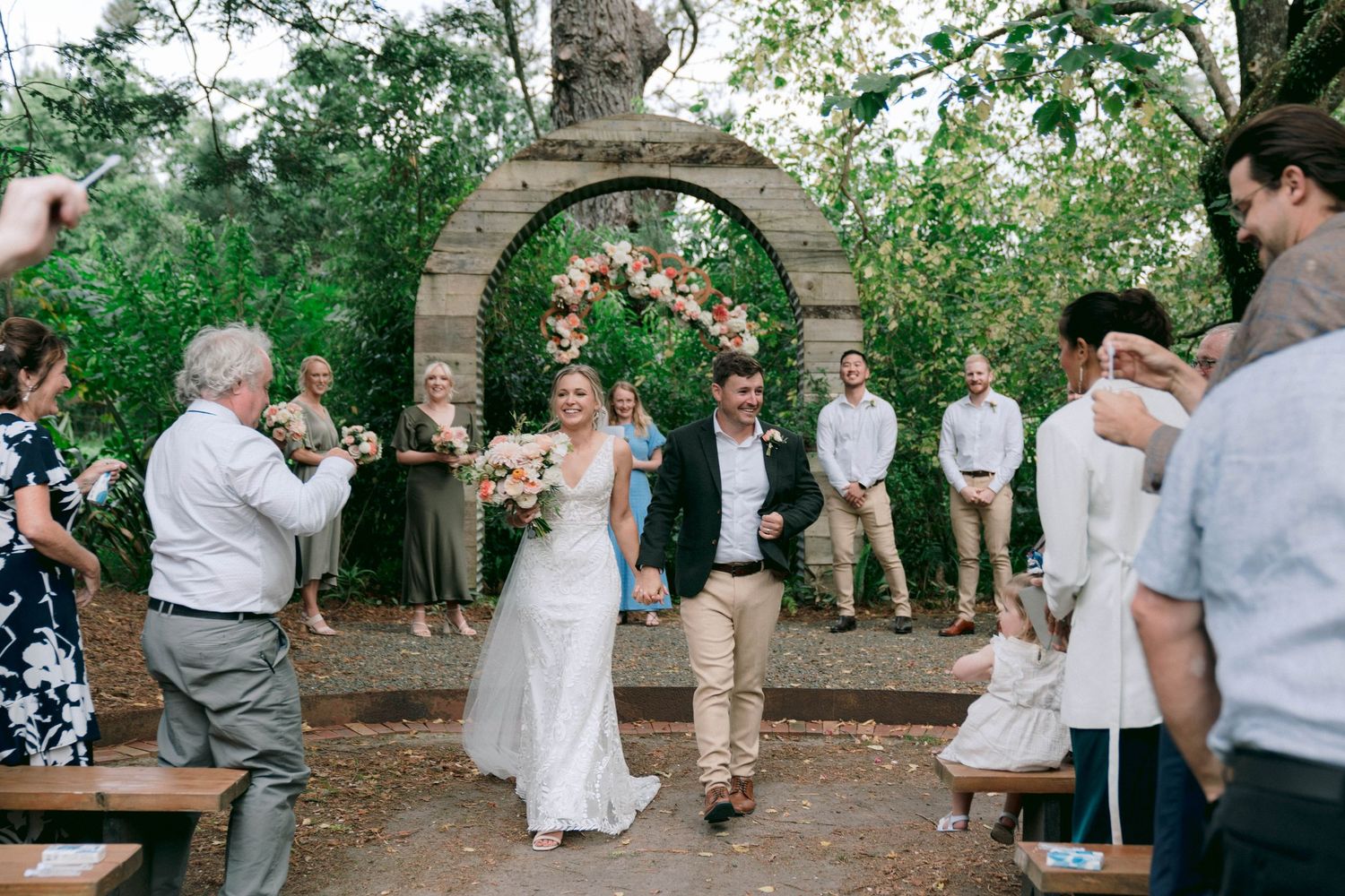 Wedding celebration taking place beneath a stone garden arch with floral decorations.