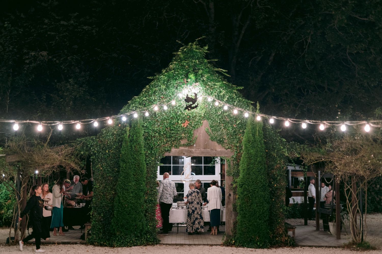 Outdoor wedding venue at night illuminated by string lights with ivy-covered walls.