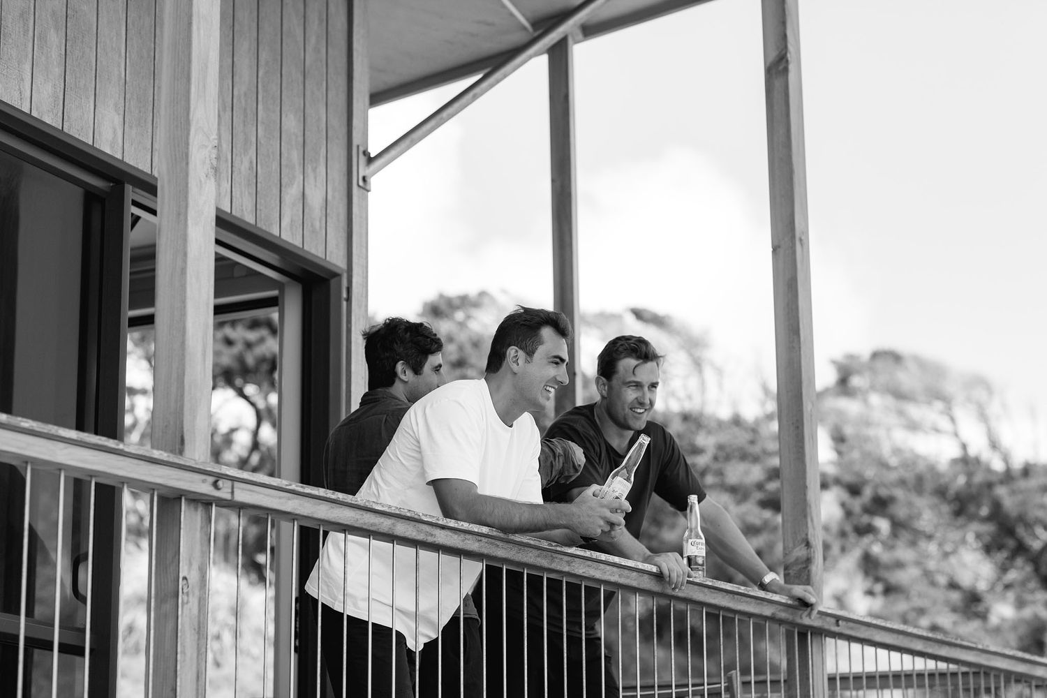 Two people lean thoughtfully on a wooden porch railing while looking at something together in black and white.