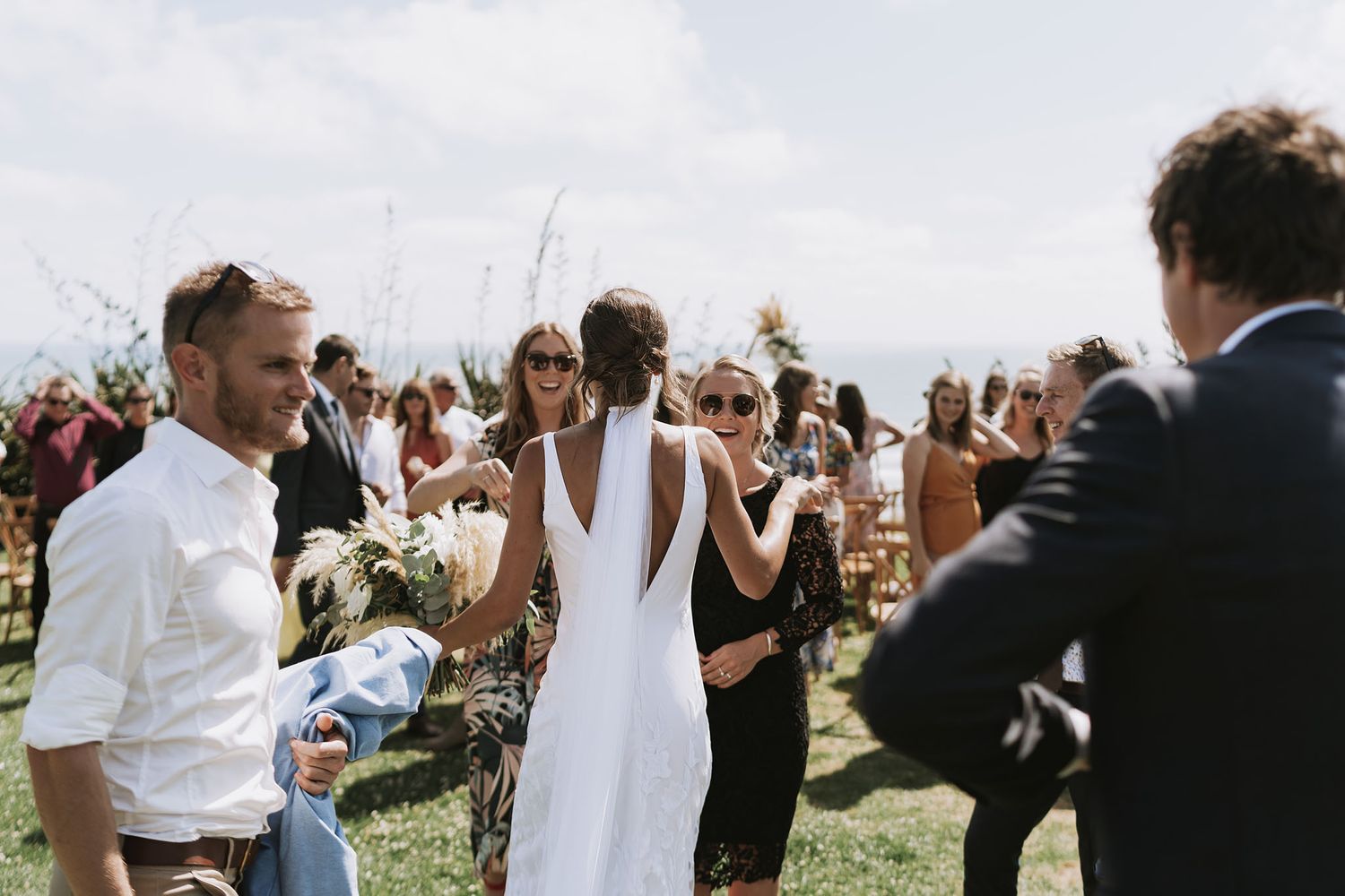 Wedding guests stand in formation raising their glasses for a celebratory toast during an outdoor reception.