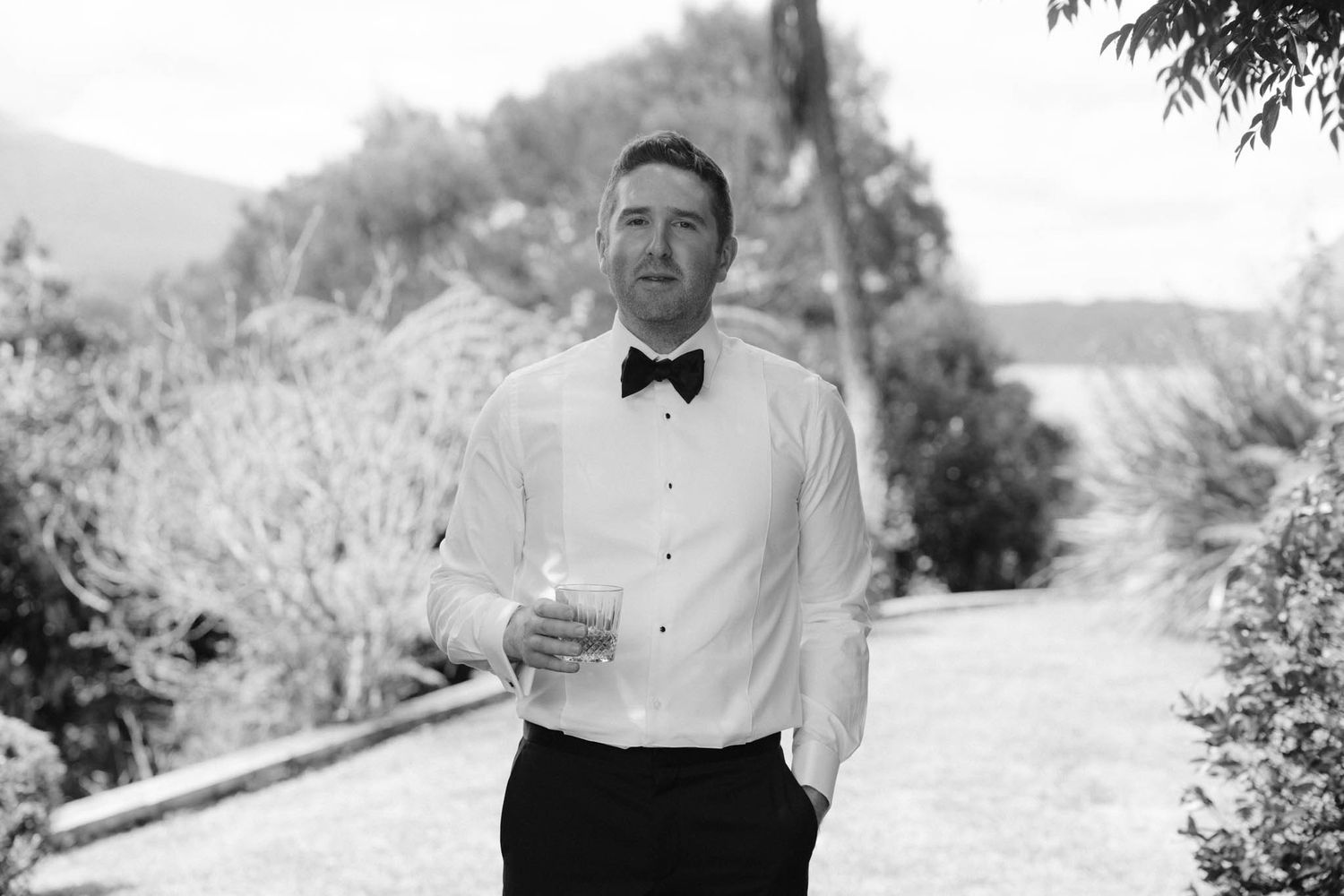 Black and white photo series showing various candid outdoor wedding party moments by a wooded lake setting.