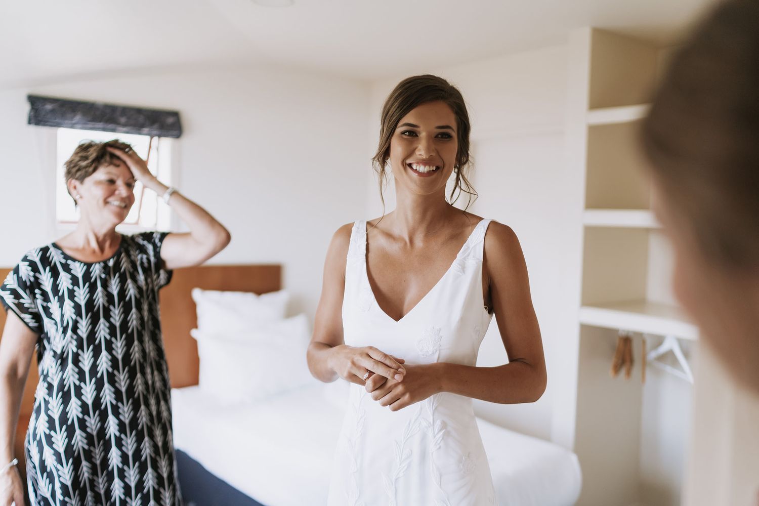 People getting ready in a bright bedroom with white bedding and natural lighting.