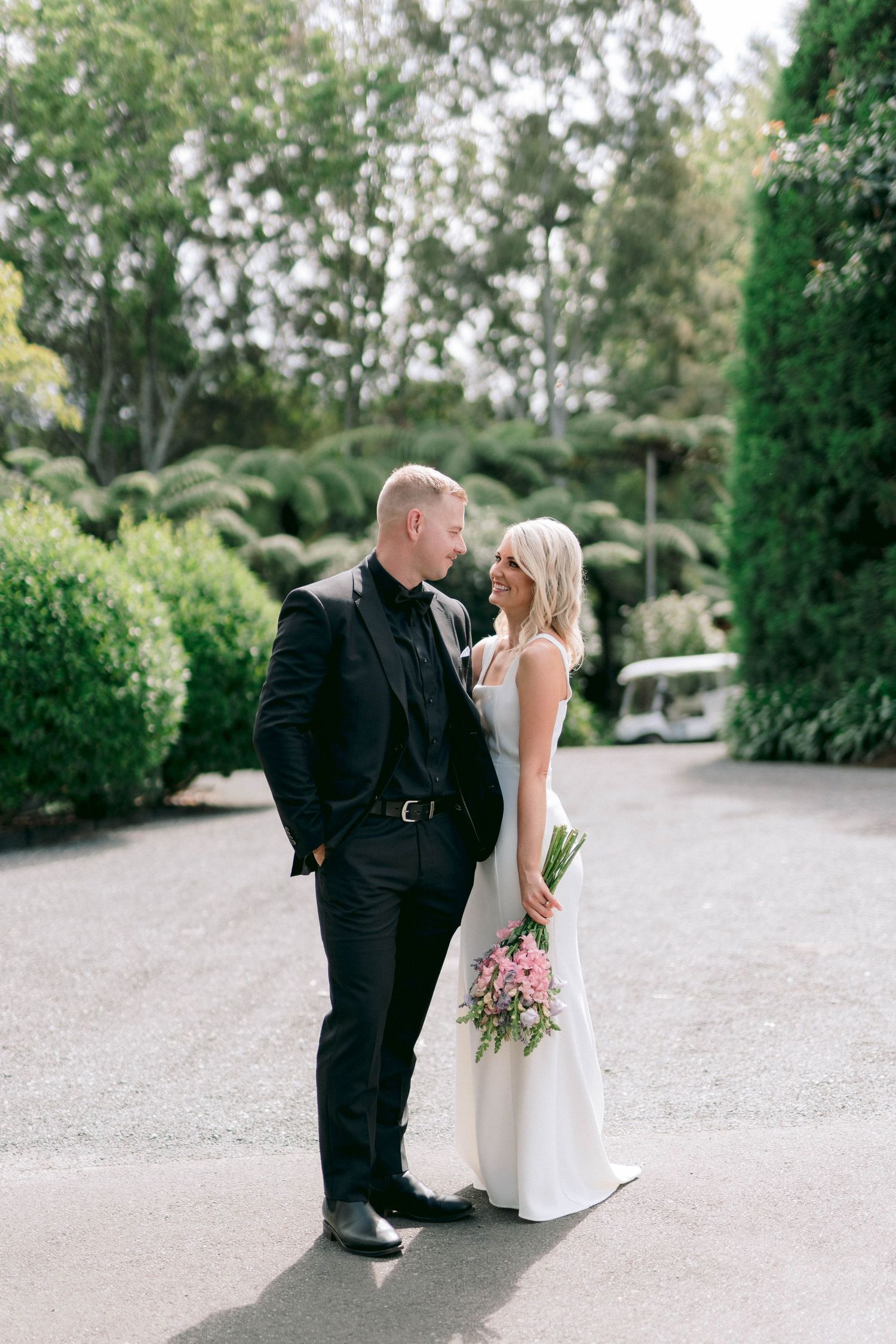 A romantic wedding photo of a couple on a garden path surrounded by lush greenery.