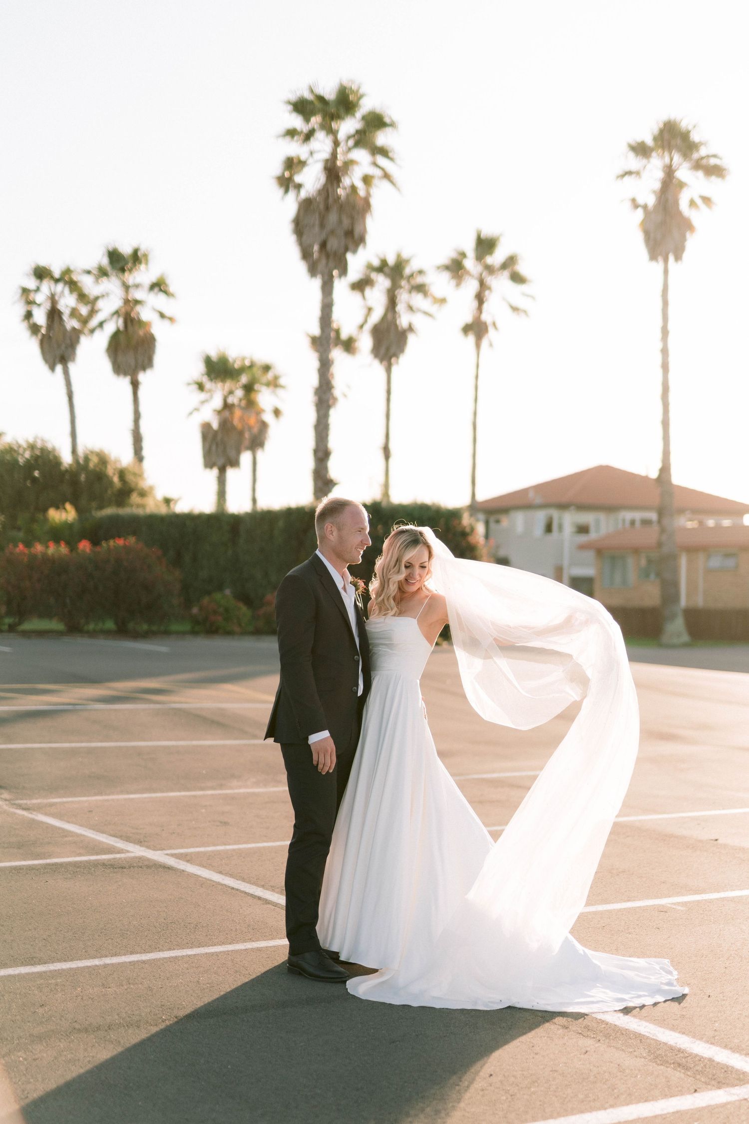 A sunset portrait with palm trees silhouetted against the sky as a wedding veil flows dramatically in the breeze.