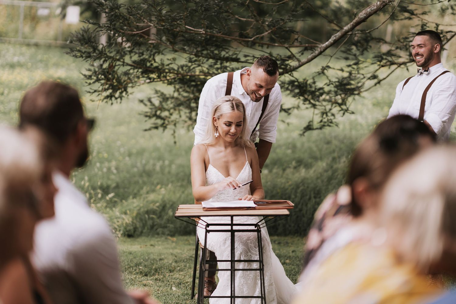 Intimate outdoor wedding ceremony with soft natural lighting and wooden chairs surrounded by green foliage.