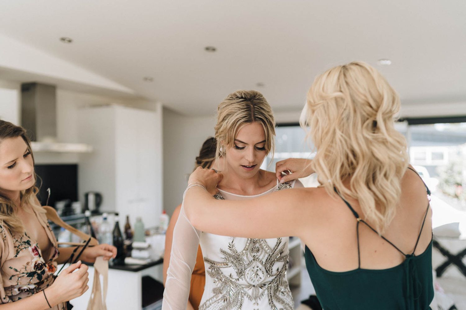 A bride getting ready for her wedding day with assistance from others in a modern kitchen setting.