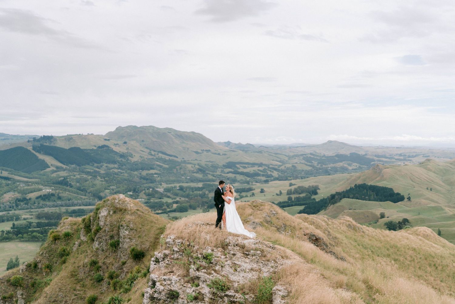 Rolling hills and mountains form a scenic backdrop for a wedding ceremony at the peak of a scenic overlook.