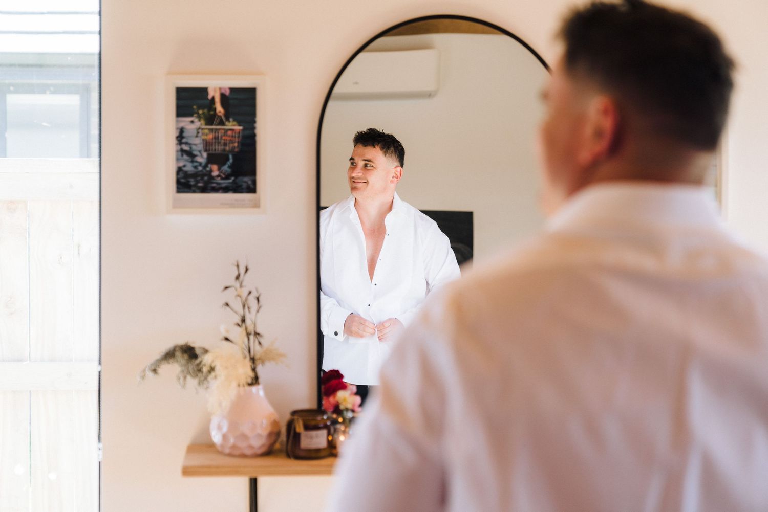 Person getting ready in front of an arched mirror with a decorative vase and minimal decor.