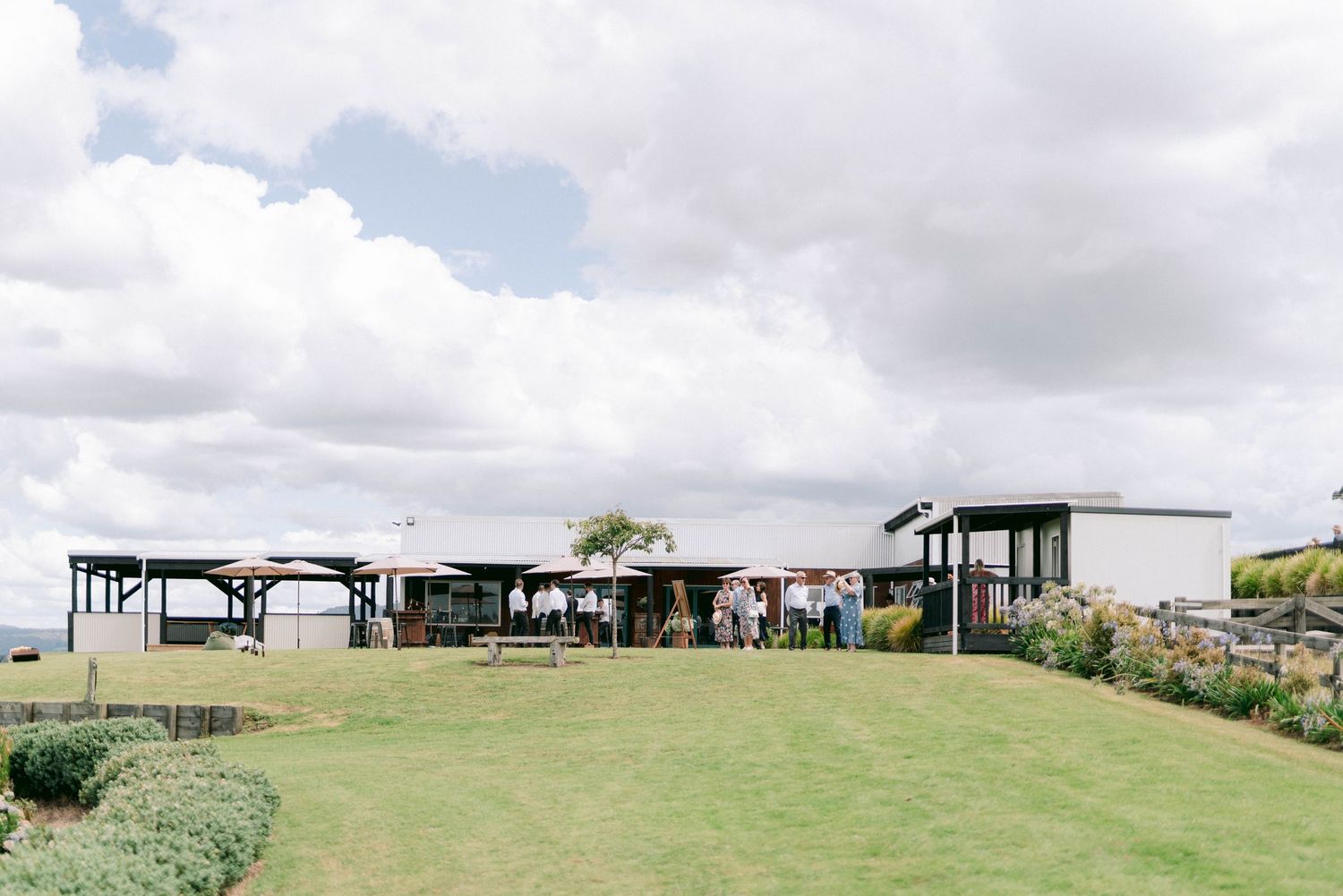 Modern outdoor pavilions with covered spaces sit atop a grassy hill under cloudy skies at a scenic venue.