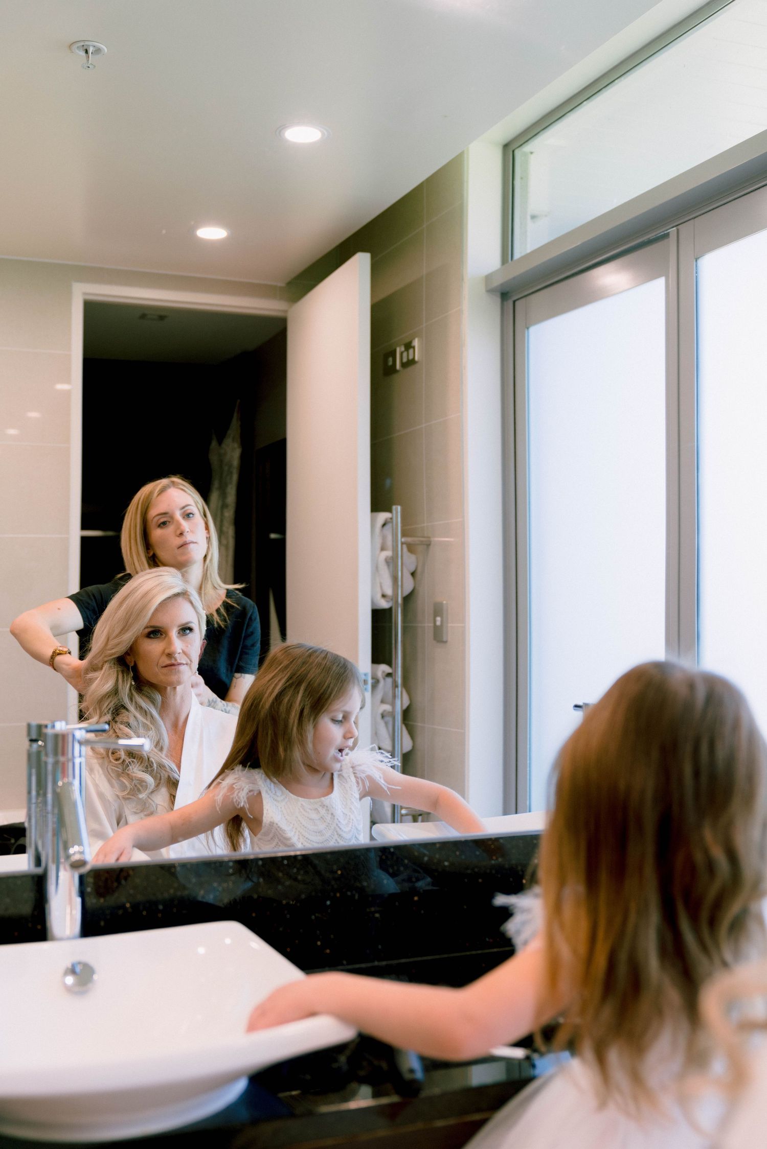 Two women getting ready in a modern bathroom with bright lighting and minimalist decor.