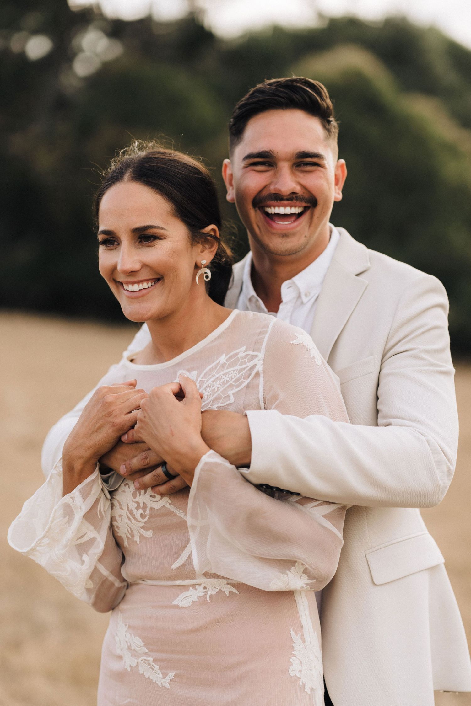 A joyful couple embraces outdoors during their wedding photoshoot, with the bride wearing a delicate lace dress.
