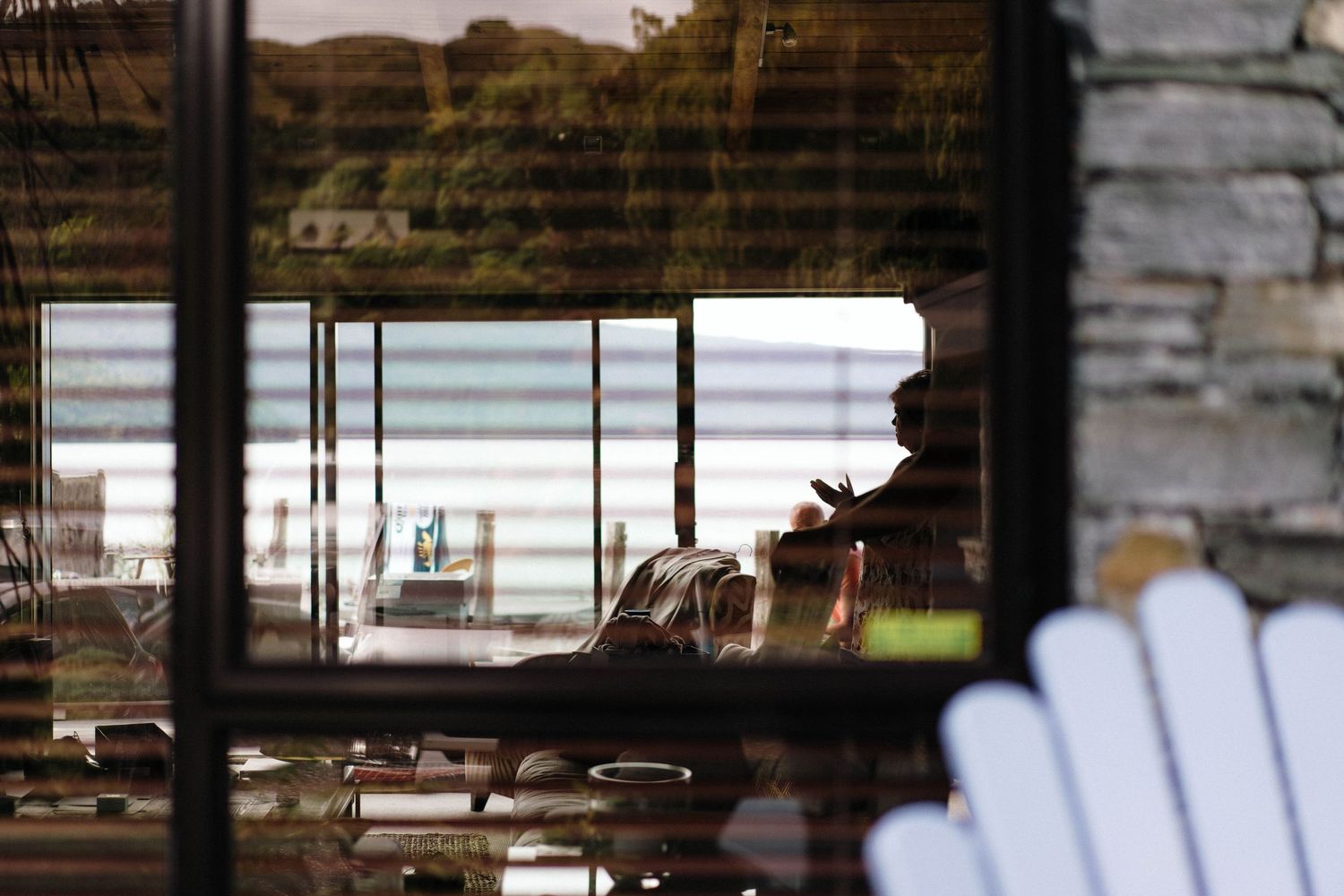 Restaurant interior scene with wooden furnishings and large windows overlooking a waterfront view.