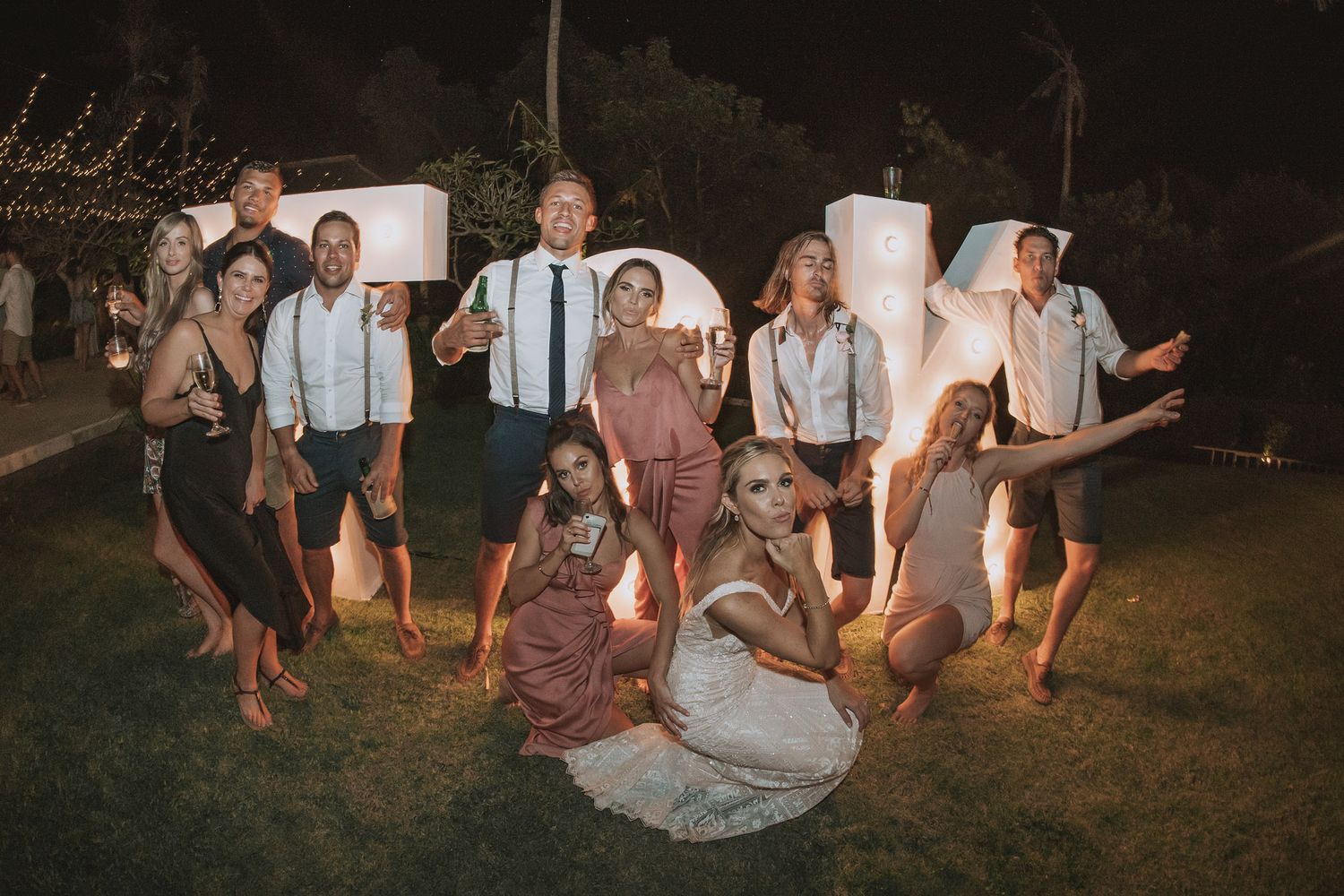Wedding party poses playfully on lawn during evening celebration.