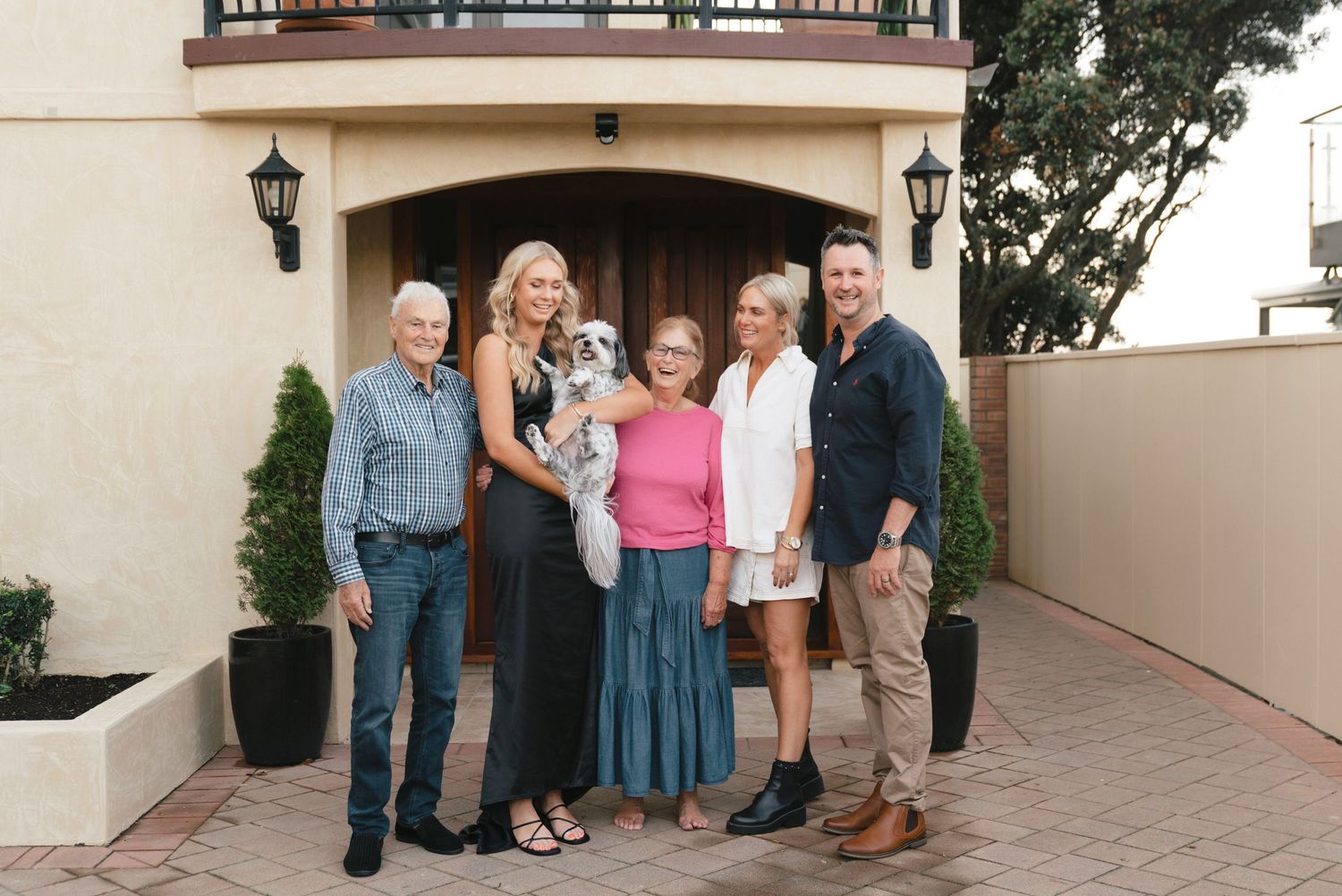 Multi-generational family gathers for portrait outside stucco home with lantern lighting.