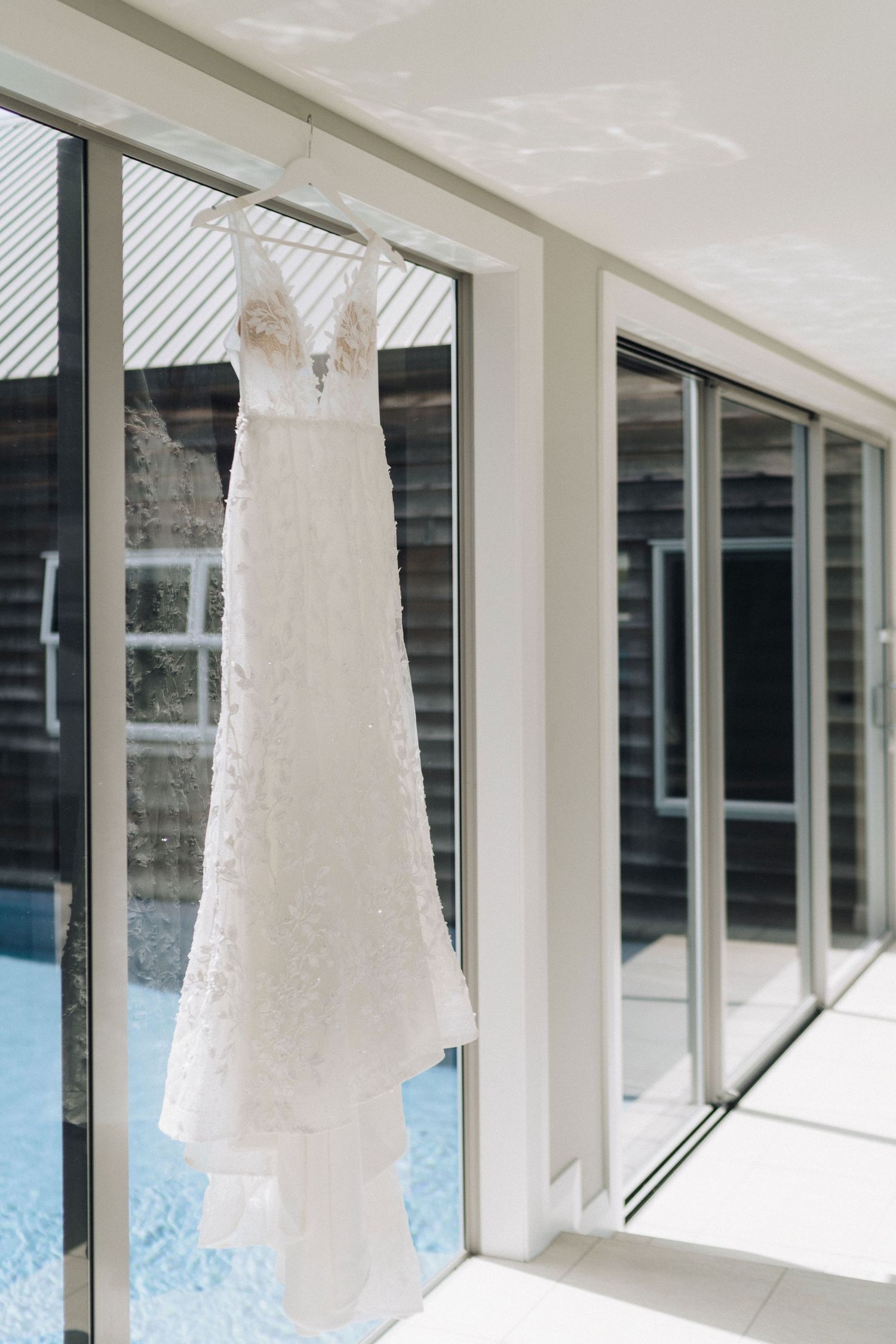 White wedding dresses hang in a row against large windows creating an elegant display.