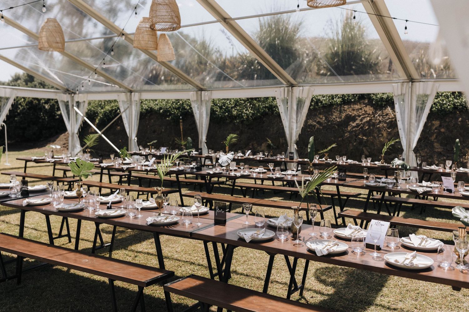 White tent reception setup with wooden picnic tables and benches in an outdoor venue.