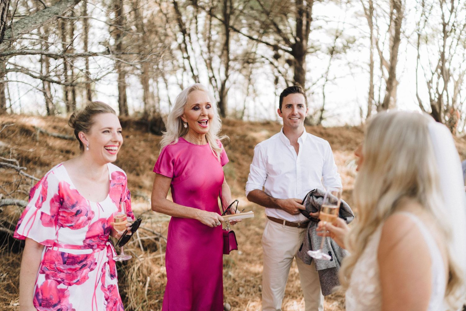 Wedding party gathered outdoors wearing bright pink and white attire.