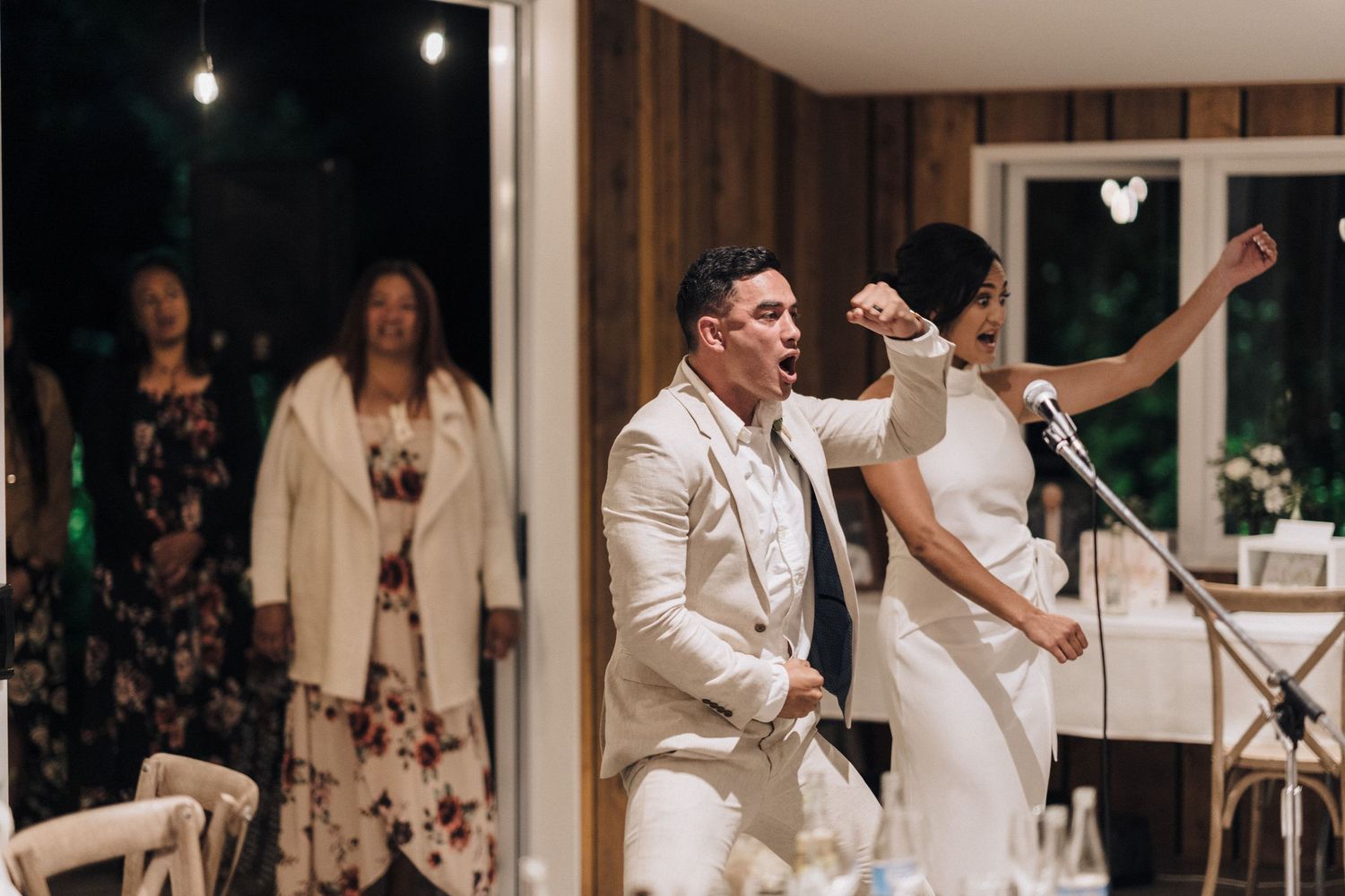 Wedding celebration at night with guests dancing and singing in formal attire.
