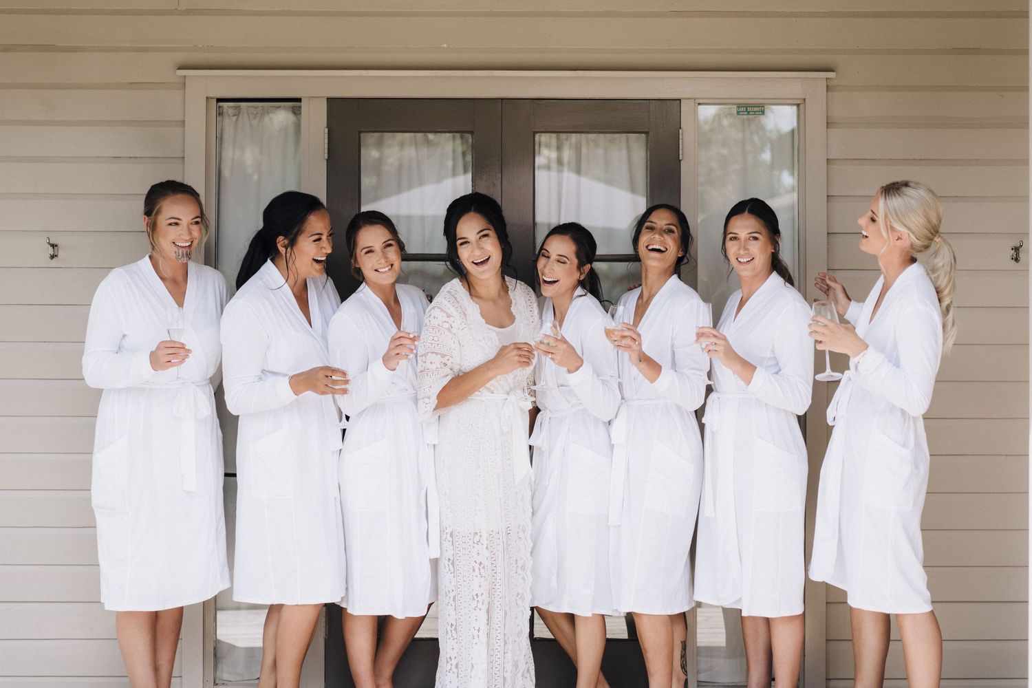 A group of people wearing matching white robes stand together against a light colored wall.