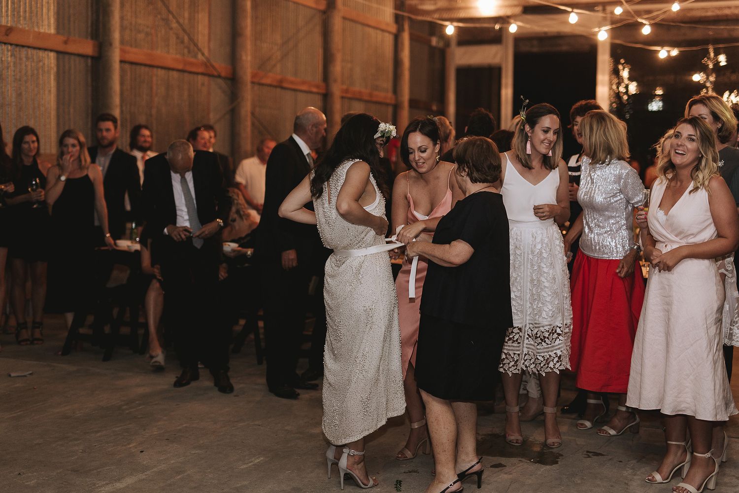 People dancing and celebrating at a dimly lit indoor reception venue with festive atmosphere.