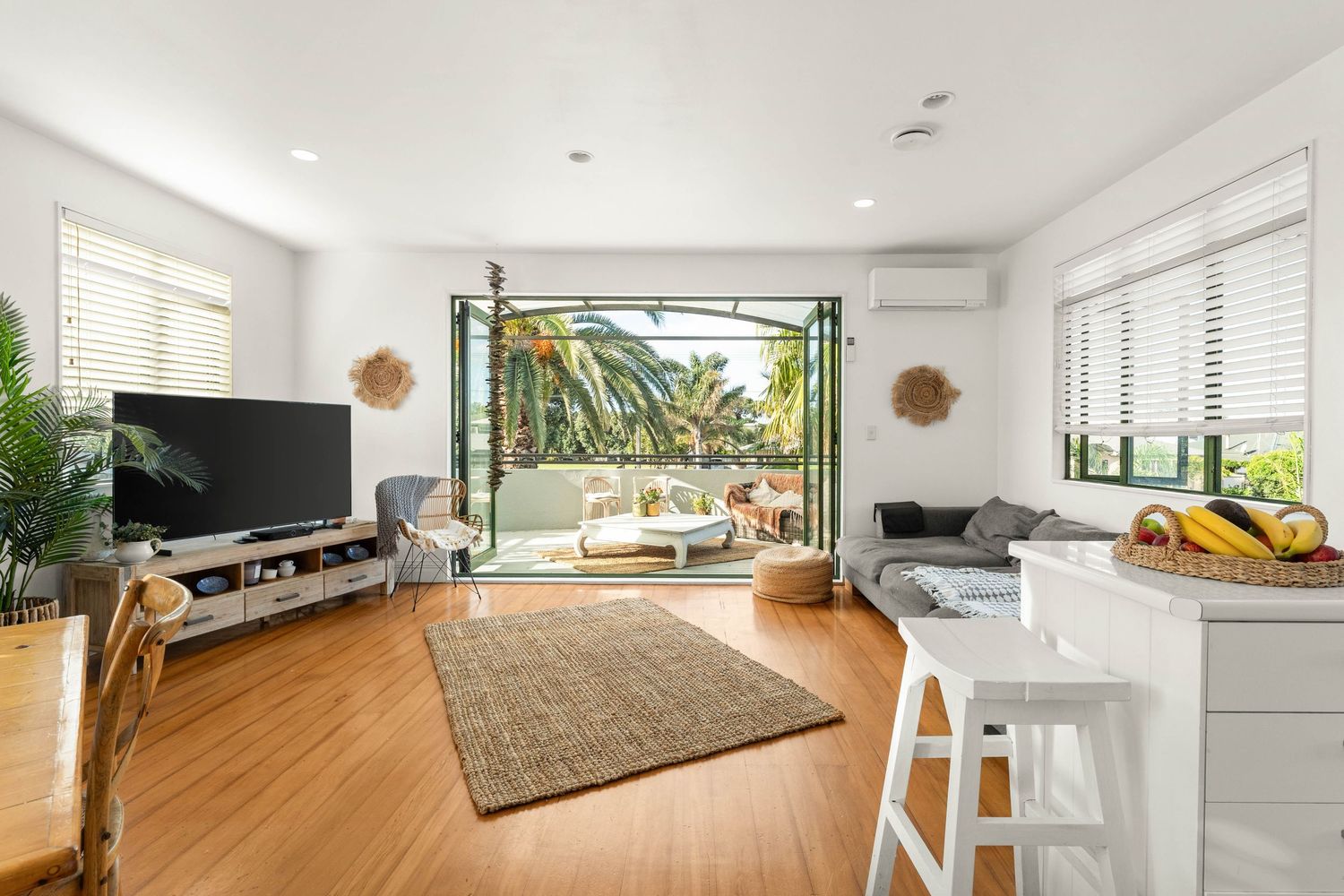 Modern white interior space with wooden flooring and large windows letting in natural light.