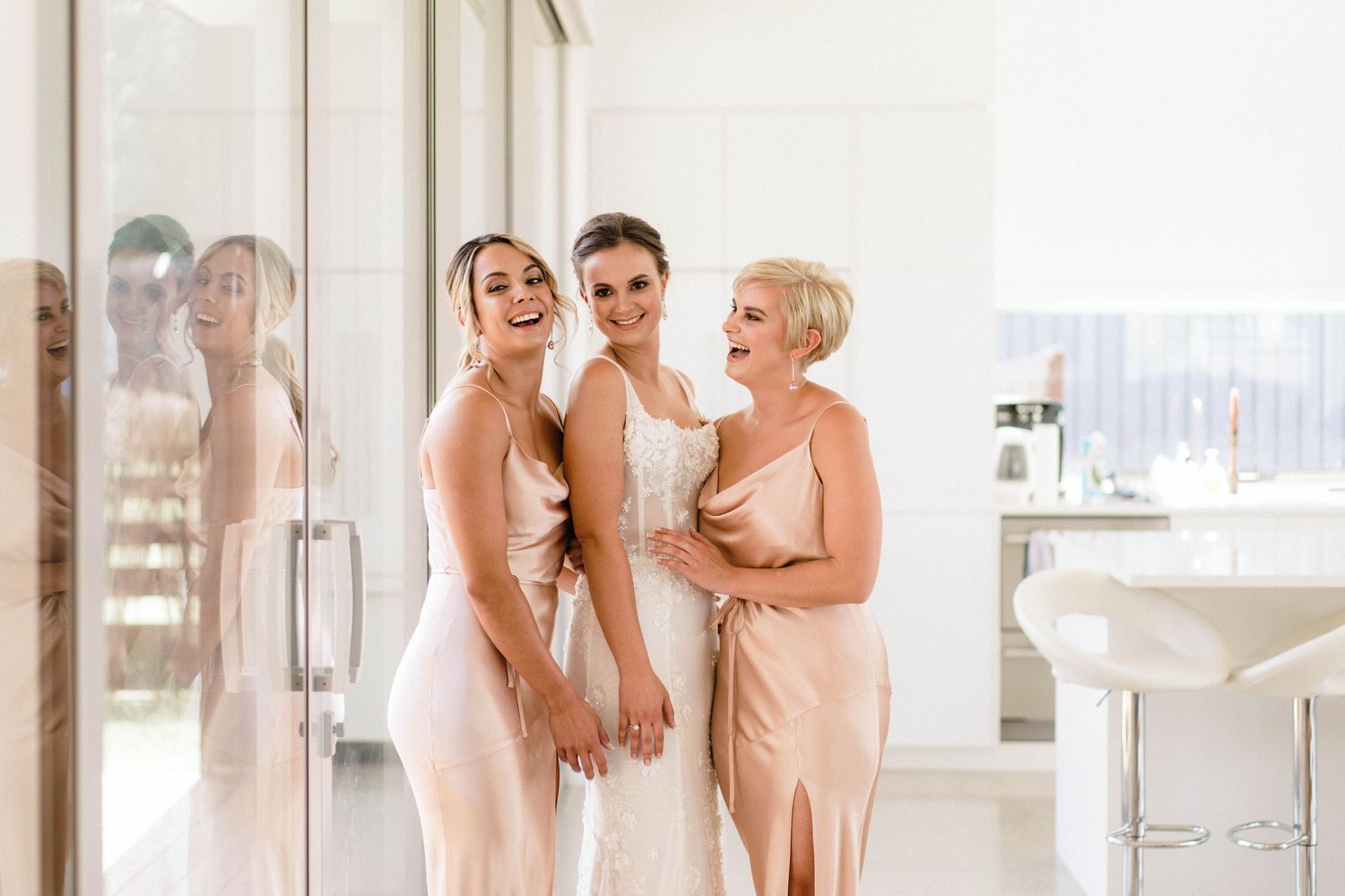 Wedding party members sharing joyful moment in elegant blush colored dresses.