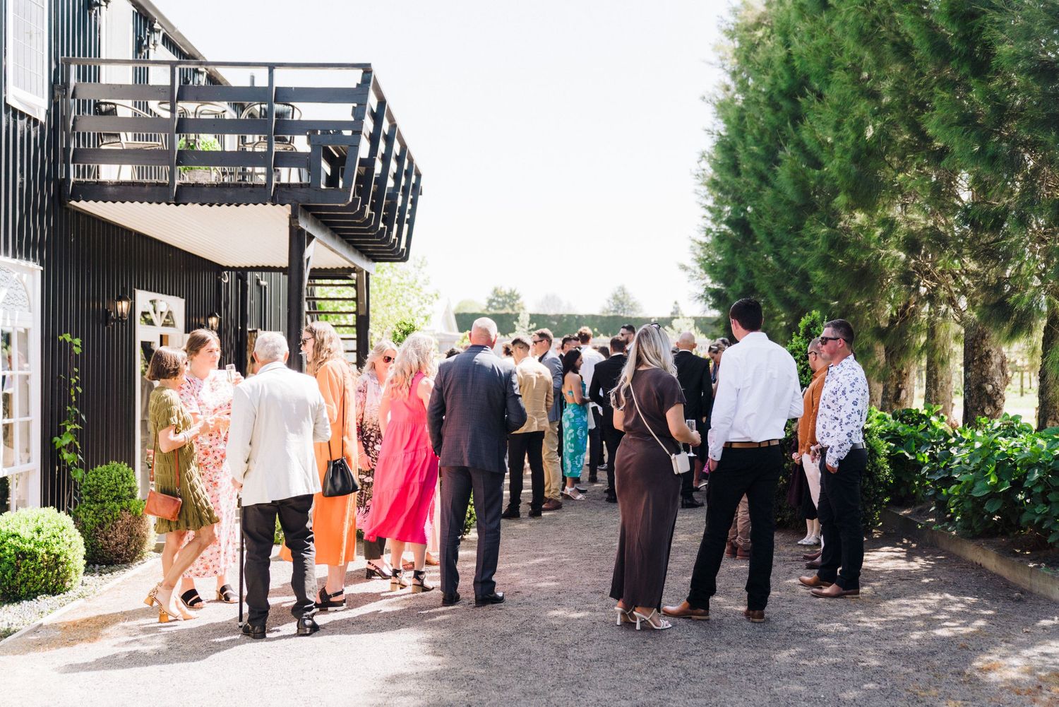 Wedding guests mingling on outdoor patio walkway during daytime event.
