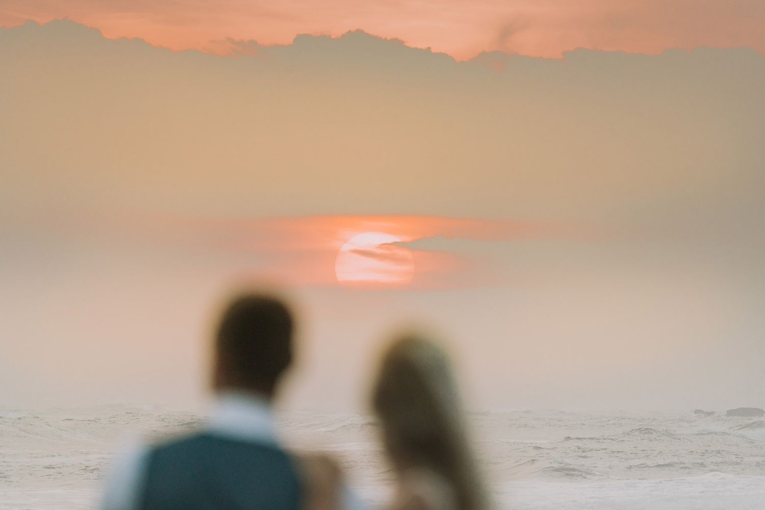 Silhouettes stand together watching a stunning orange sunset over the ocean horizon.
