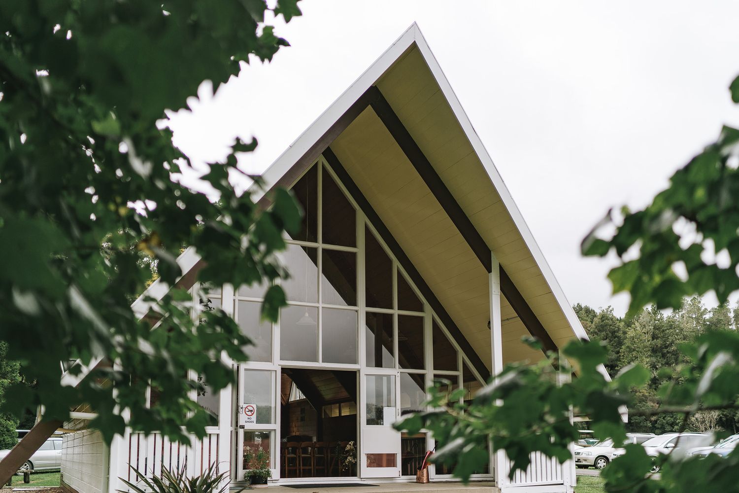 Modern A-frame church with white exterior and dramatic angled roof peaks through green summer foliage.