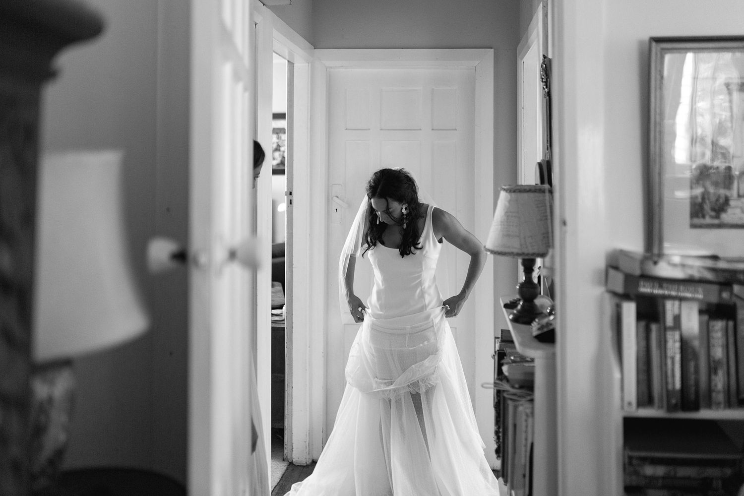 A figure in a white wedding dress stands near a bright window in an elegant residential hallway.