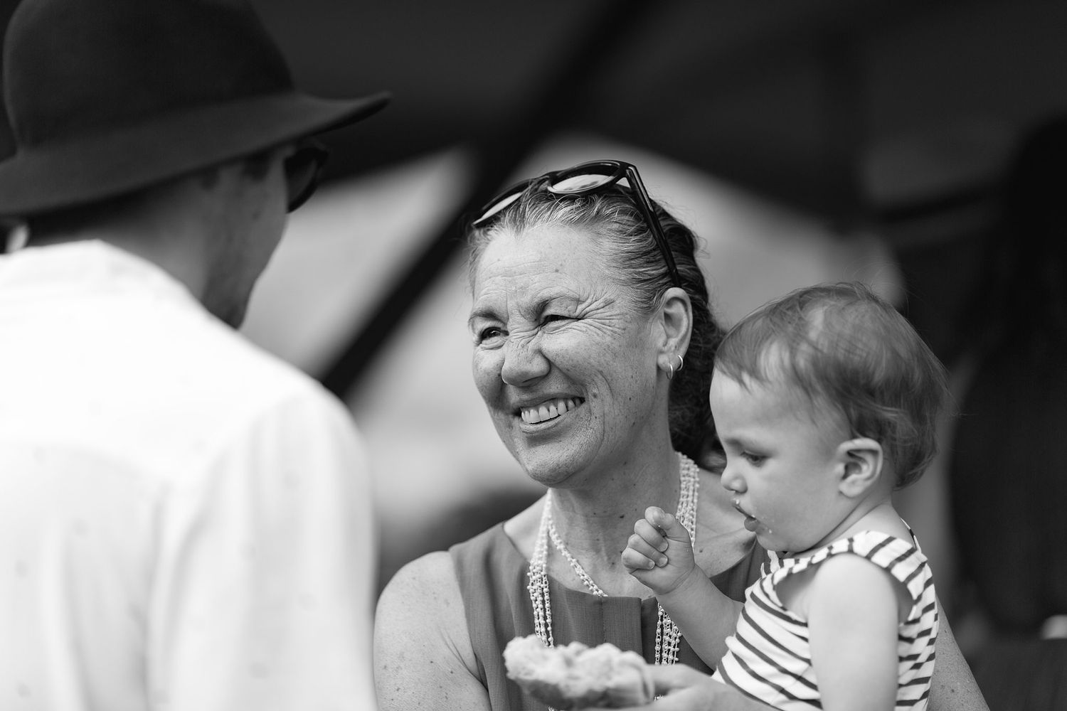 A candid black and white moment showing joyful laughter shared between people with a small child at an outdoor gathering.